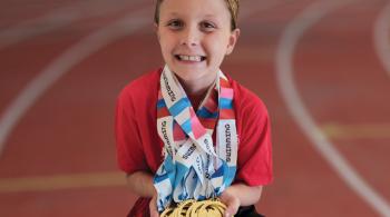 Penelope, smiling, wears nine medals around her neck, all of them gold, and with red, white and blue ribbons. Some of the ribbons can be seen to say “SWIMMING” on them.