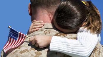 A soldier carries his young daughter, who is wrapping her arms around his soldiers while holding a small United States flag.