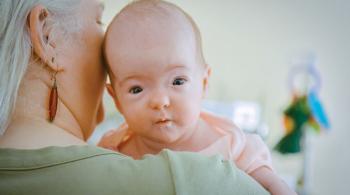 A baby rests its head on a woman's shoulder while being held.