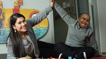 A teacher and a young boy high-five each other while playing with Lego bricks.