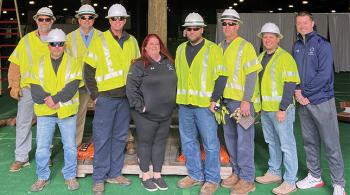 A group of nine people, mostly men and mostly wearing bright yellow construction vests and helmets, pose for the camera.