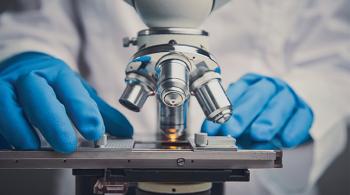 Two latex-gloved hands operate a microscope.