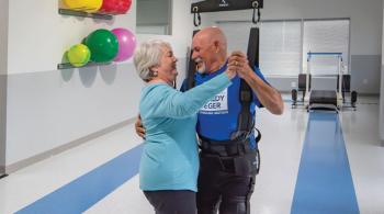 A woman and a man share a dance in a gym setting. The man is in a harness that is attached to the ceiling and holding him up.