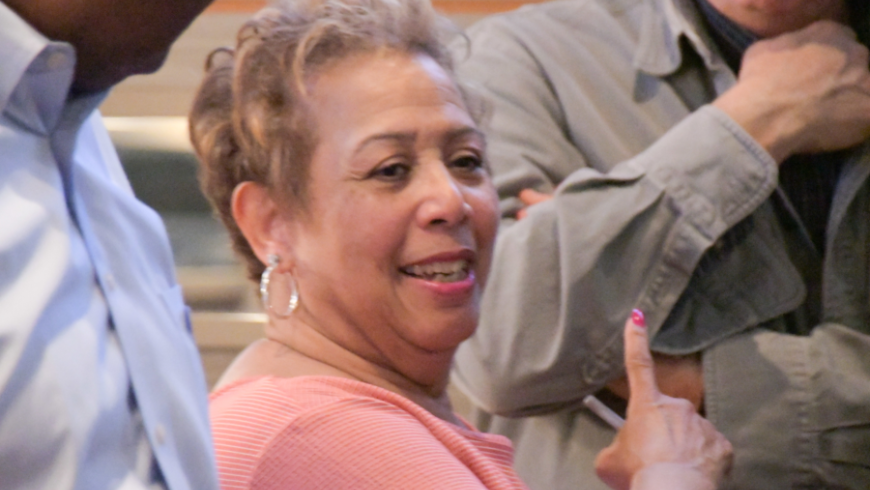 Closeup image of a woman in a pink shirt speaking with other attendees. 